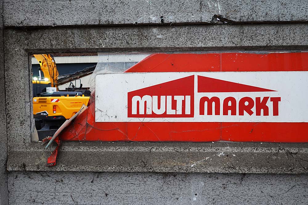 Medewerkers Poiesz van gevel gehaaldMet het weghalen van de meer dan levensgrote portretten van medewerkers op de buitengevel komt een einde aan de "oude" Poiesz in Akkrum. Ze verdwijnen in het sloopmateriaal. Na het verwijderen van een laatste beetje asbest maandag zit de vaart er nu goed in. Met een mobiele kraan en grijper zijn de muren van de supermarkt rondom omver gehaald. Ook de houten kozijnen met daarin de portretten zijn maandag vrijwel allemaal weggehaald.Met een week hoopt Van der Wal Sloopwerken klaar te zijn. Daarna volgt de sanering van de grond, die als gevolg van een benzinepomp van garage Fennema in het verleden vervuild is geraakt. Daarmee komt een eind aan de vestiging van een supermarkt op die plek. Na de verhuizing verhuurde Fennema het pand aan groothandel Flevozoom, die er in de eerste helft van de jaren tachtig een Multimarkt in onderbracht. Rikus Rudolphi werd daar toen bedrijfsleider. Later werd de Multimarkt in een Golff-supermarkt omgeturnd. Na verschillende verbouwingen en ook een poosje de verkoop van fietsen nam Poiesz-supermarkt in 2005 de winkel over.                