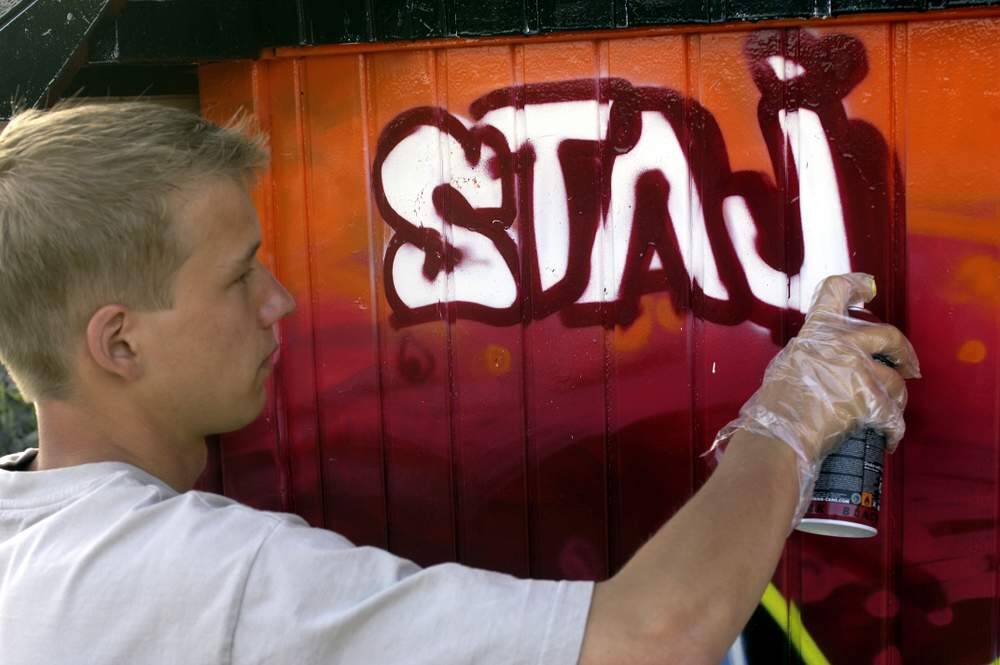 Een van de bezoekers van het jongerenwerk in Akkrum schildert het logo van de stichting STAJ op de muur van de compeet vernieuwde soos, een voormalige directiekeet.